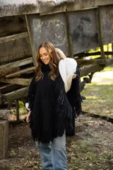 Poncho de lana merino color negro, con cuello alto, diseño amplio y terminaciones con flecos en todo el borde.