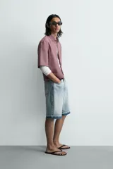 Bermuda de denim de algodón con efecto lavado desgastado en tonos marrones y azules. Tiene tiro medio, diseño de cinco bolsillos, pierna recta de corte holgado y bajo con acabado irregular. Cuenta con cierre frontal de cremallera y botón metálico.