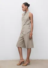Top color beige, con cuello drapeado, diseño sin mangas, espalda abierta con cierre de lazo y dobladillo asimétrico.
