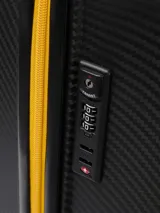 Valija rígida color negro con textura de fibra de carbono y detalles en amarillo. Cuenta con cuatro ruedas dobles, carro extensible y cierre principal con detalles en contraste.