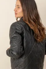 Campera de cuero negro estilo capitoneada, con diseño acolchado de rombos, cuello camisero, cierre frontal con botones a presión y bolsillos laterales.