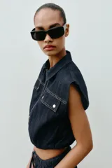 Chaleco de denim oscuro con cuello solapa, cierre frontal con cremallera metálica y bolsillos delanteros con tapeta. Presenta un diseño de corte abullonado con bajo elástico.