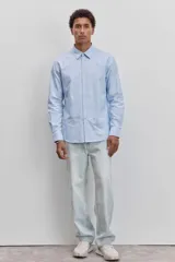 Camisa de manga larga en color celeste, con cuello clásico y cierre frontal de botones. Presenta un diseño de corte recto y acabado liso.