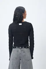 Top tejido negro con trama calada, escote en V, frunce central regulable y mangas acampanadas.