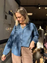 Camisa de popelina color azul, con cuello en V, cierre frontal con botones y diseño de volados laterales y en los puños.