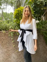 Camisola blanca con escote en V, mangas 3/4 y lazo negro en la cintura.