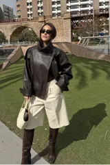 Chaqueta de efecto cuero con cuello alto, cierre frontal cruzado con botones a presión, hombreras y cintura elástica. Presenta un acabado texturizado y bolsillos laterales.