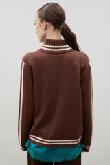 Campera tejida de punto color marrón con cierre frontal completo, cuello alto y detalles de rayas blancas en cuello, puños y ruedo. Presenta el logo de la marca estampado en el frente.