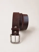 Cinturón marrón de cuero con diseño texturizado en relieve tipo damero, hebilla metálica rectangular plateada envejecida y trabilla a juego fijada con remaches metálicos.