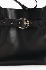 Cartera tote negra de tejido revestido, con cierre magnético y correa de hombro ajustable. Presenta una correa decorativa exterior con hebilla metálica dorada y ojetes alrededor, además de compartimento interior con cierre y forrería.