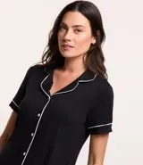 Conjunto de pijama corto negro con ribetes blancos, compuesto por una camisa de manga corta con cuello, bolsillo en el pecho y cierre abotonado, y un short con cintura elástica.