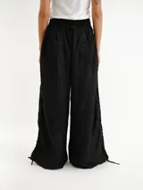 Pantalón negro de lino con cintura elástica fruncida y pernera ancha, con detalles de cordones ajustables a los lados.