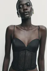Top estilo corset con copas de tejido satinado y cuerpo de encaje semitransparente con varillas. Presenta tirantes finos ajustables y cierre lateral con cremallera oculta.