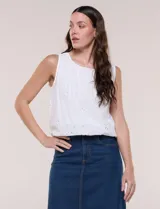 Blusa blanca sin mangas de calce holgado, confeccionada en tejido liviano con bordado estilo broderie. Presenta escote bote y ruedo inferior elastizado que genera un sutil efecto abullonado.