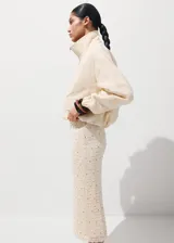 Falda midi de corte recto, confeccionada en tejido texturizado de color beige con pequeñas tachas metálicas distribuidas en el diseño y forro interior.