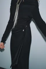 Vestido largo de color marrón oscuro, con cuello fluido tipo bote, manga larga y detalle de fruncido lateral con broche metálico en la cintura.