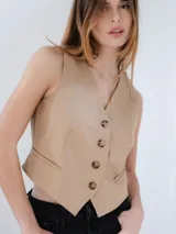 Chaleco sastrero color beige, con escote en V, cierre frontal con botones y bolsillos laterales decorativos.