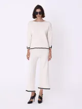 Conjunto de dos piezas de tejido de punto en color blanco con detalles de bordes en negro. Incluye un sweater de corte recto con mangas tres cuartos y un pantalón de corte amplio y largo cropped.