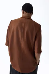 Blazer de manga corta de botonadura sencilla en color marrón, con solapas de muesca, cierre de un botón frontal, bolsillos delanteros ribeteados y forro interior.