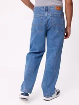 Jean de corte slouchy fit, confeccionado en denim de algodón color azul medio. Presenta diseño de cinco bolsillos, cierre frontal con botón y costuras reforzadas en tono contrastante.