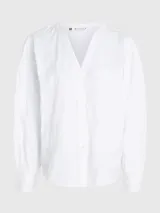 Blusa blanca de algodón orgánico con cuello en V, mangas largas abullonadas con puños abotonados y detalles de encaje vertical.