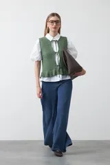 Chaleco tejido color verde musgo, con trama texturada, cuello a la base y cierre frontal con lazos. Presenta un ruedo con volado.