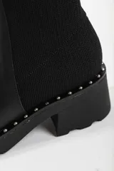 Bota de caña media color negro, con diseño tipo chelsea, suela track con detalle de tachas metálicas en el borde y elástico lateral.