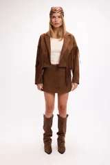 Chaqueta de efecto gamuza en color marrón, con solapas amplias, cierre frontal con botón y flecos largos decorativos en la parte frontal y trasera. Presenta un diseño estructurado de estilo western.