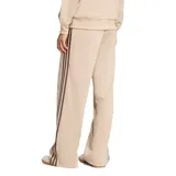 Pantalón deportivo Adidas de corte holgado, color beige con las tres tiras características en los laterales en tono marrón. Presenta diseño de pierna recta, bolsillos laterales y logo de la marca bordado.