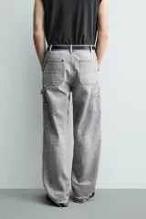 Pantalón de jean estilo carpintero con corte relaxed fit, tiro medio y pierna recta. Presenta un lavado azul medio con efecto desgastado y roturas en las rodillas. Incluye bolsillos laterales tipo plastrón, tira multifunción en la pierna, cierre frontal con cremallera y botón.