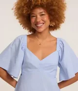 Vestido corto evasé color celeste, con escote en V, mangas cortas amplias, recorte cutout en los laterales de la cintura y volado en el bajo.