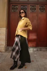 Falda midi de diseño asimétrico que combina un panel de tela escocesa en tonos verdes, blancos y marrones con un panel lateral de paño verde oscuro. Presenta un tajo lateral pronunciado y tiro a la cintura.