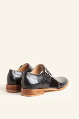Zapato tipo oxford abierto en los laterales, confeccionado en cuero vacuno negro. Presenta doble tira con hebillas metálicas en el empeine y detalle de tachas plateadas en el contorno del talón y la puntera.