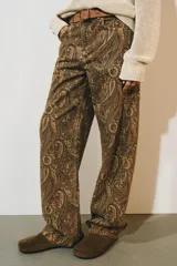 Jeans de tiro medio con diseño de perneras curvas y corte recto, confeccionados en denim con estampado paisley en tonos marrones y beige. Presentan diseño clásico de cinco bolsillos, trabillas para cinturón y cierre frontal con cremallera y botón metálico.