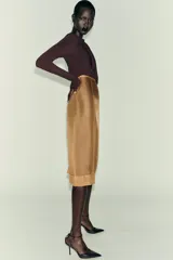 Body de manga larga color marrón oscuro, con escote asimétrico drapeado y detalle de broche metálico en el hombro derecho.