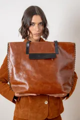 Bolso tipo shopper de cuero vacuno color chocolate con textura efecto croco. Presenta detalles de pasamanería en los laterales, cierre superior y una borla decorativa de flecos de cuero.