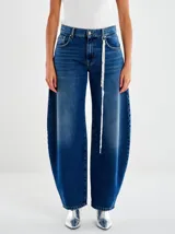 Jeans de denim azul oscuro con efecto degradado (ombré) que se aclara hacia los tobillos. Tienen un corte extremadamente holgado y redondeado (balloon/bomba) y un cordón blanco decorativo colgando del bolsillo delantero.