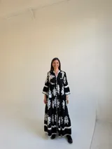 Vestido largo negro con estampado floral blanco, escote en V con cuello mao, cierre frontal de botones y mangas tres cuartos acampanadas.