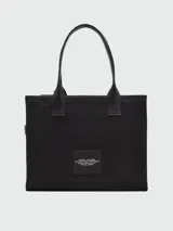 Bolso tipo tote Marc Jacobs modelo The Cargo Canvas Large Tote Bag, color tostado, confeccionado en lona con múltiples bolsillos delanteros con solapa y cierre, detalle de anilla metálica y estampado gráfico con el nombre de la marca. Cuenta con asas dobles para el hombro.