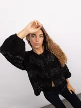 Campera de punto con cierre frontal bidireccional, mangas largas abullonadas y diseño calado con patrón de ondas en color negro con detalles brillantes.