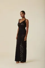 Vestido largo de encaje negro con escote en V y breteles anchos. Presenta un diseño ajustado en el torso que cae con fluidez hacia el ruedo, con una transparencia característica del tejido.