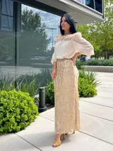Falda larga color beige con sobrecapa de encaje dorado con diseño floral o arabesco.