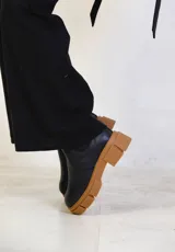 Botas tipo chelsea de cuero negro con textura granulada, paneles laterales elásticos y suela track de goma color suela con plataforma.
