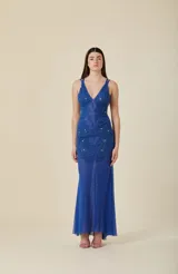 Vestido largo de tul elastizado color azul, con escote en V y tirantes finos. Presenta apliques bordados a mano y detalles de canutillos al tono en el torso, con una falda de caída suave y fluida.