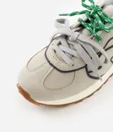 Championes de estilo retro inspirados en botines de fútbol, con capellada de poliuretano en color beige y detalles en azul marino. Presentan suela tractorada color caramelo, refuerzo en el talón y cordones combinados en gris y verde.