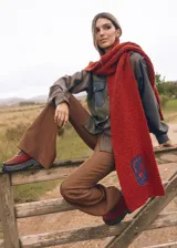 Bufanda tejida a mano de punto grueso color rojo ladrillo, con un parche bordado en el extremo que muestra un caballo y la frase "The Ranch Dress Code".