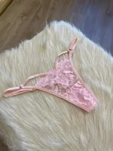 Tanga de encaje color rosa con diseño de tiras laterales regulables y detalle de elásticos.
