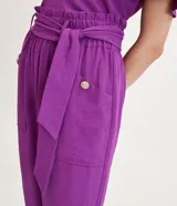 Pantalón pantacourt color violeta con cintura elástica, lazo en la cintura, bolsillos con botones y textura airflow.