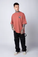 Remera de corte oversize color terracota, con cuello redondo y manga corta. Presenta un estampado circular pequeño en el pecho con motivos orientales.