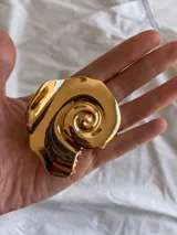 Pinza para el pelo con forma de caracola en espiral, de color dorado con acabado brillante y fabricada en aleación de metal.